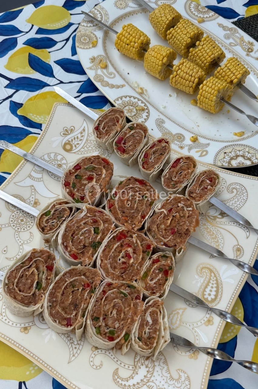 Assortiment de roulés apéritifs au thon et légumes sur assiette, accompagné d'épis de maïs grillés.