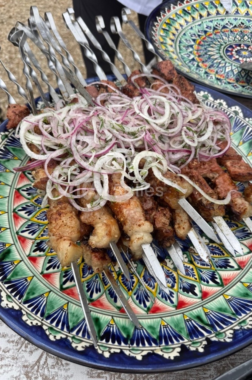 Brochettes de viande grillée garnies d'oignons émincés, présentées sur une assiette colorée.