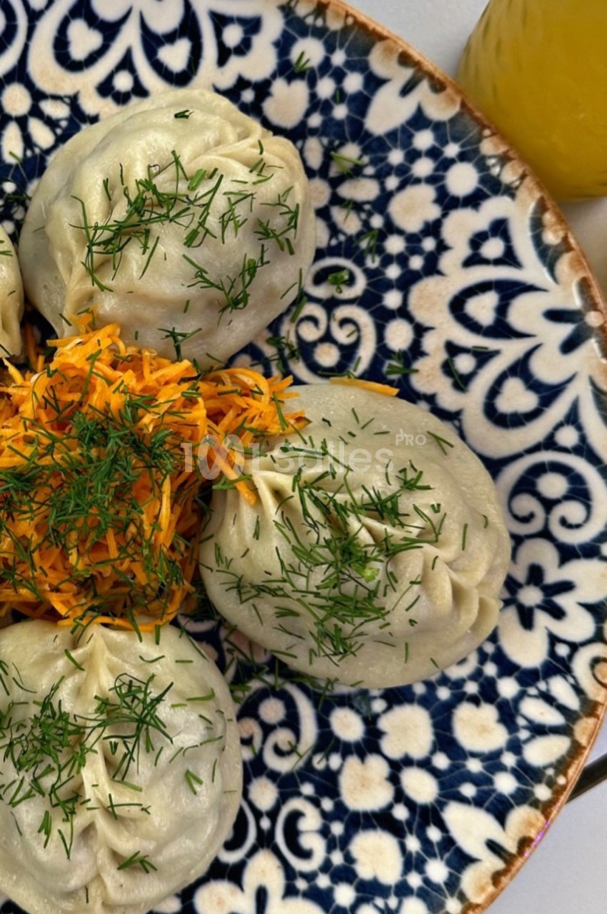 Assiette de raviolis garnis d'aneth accompagnés de carottes râpées, présentée sur un plat à motifs bleus.
