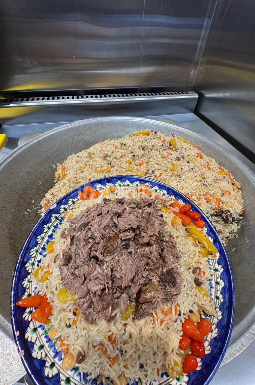 Plat de riz garni de légumes colorés et de morceaux de viande, présenté dans un grand plat décoré.