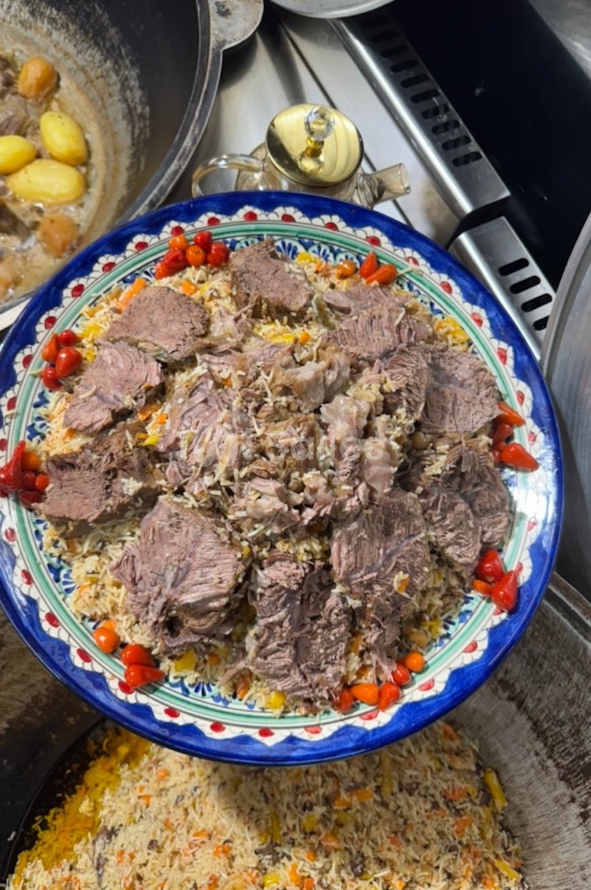 Plat de riz garni de morceaux de viande cuite, décoré de petits légumes rouges, présenté dans un grand plat coloré.