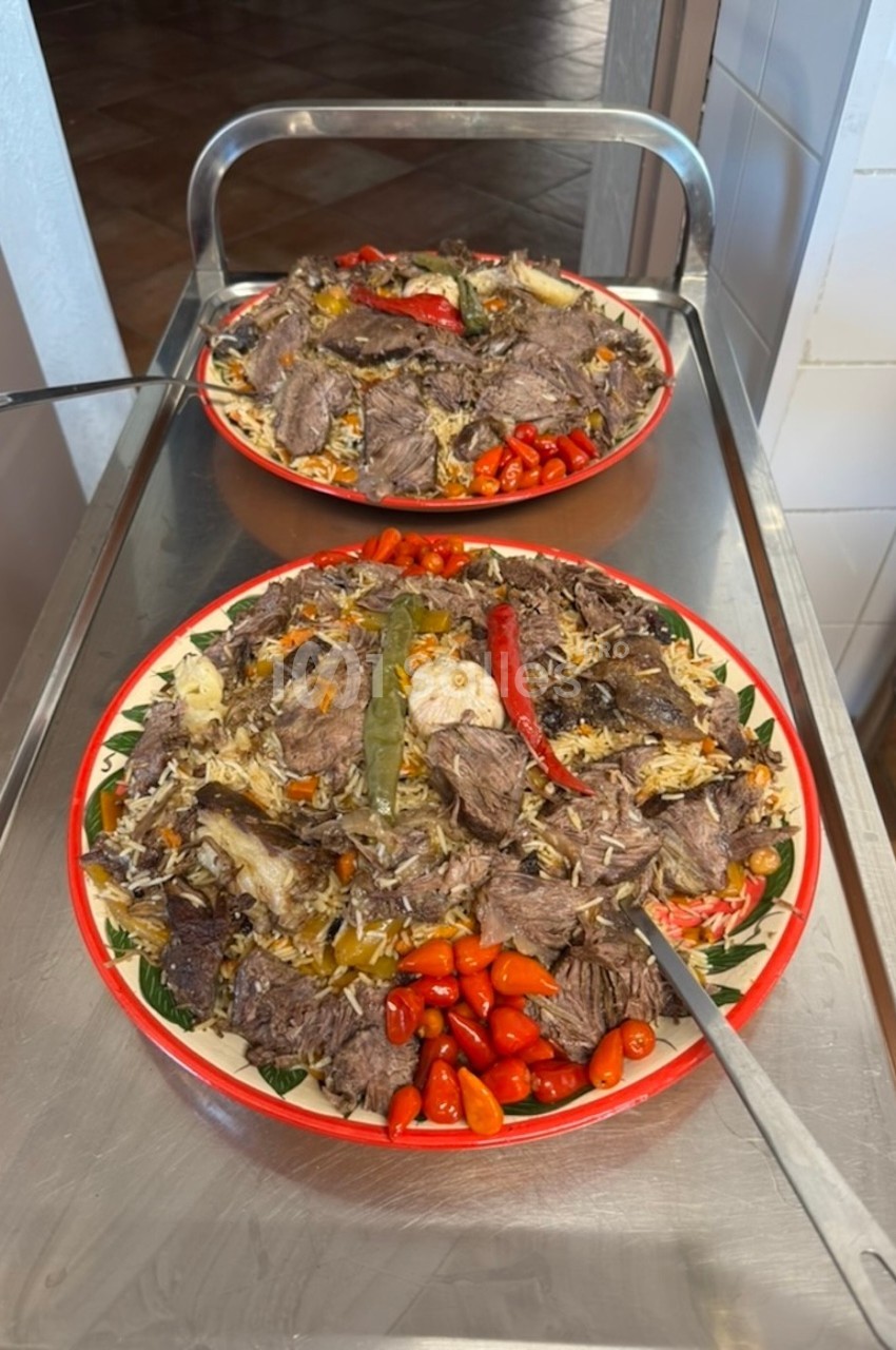 Deux grands plats de riz garnis de morceaux de viande, légumes variés et piments rouges, posés sur un chariot en métal.