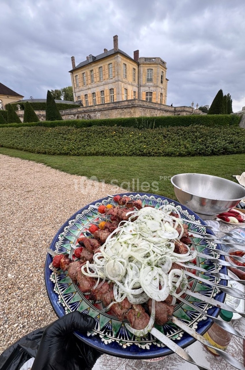Assiette de brochettes garnies d'oignons et de légumes devant un château entouré de jardins.