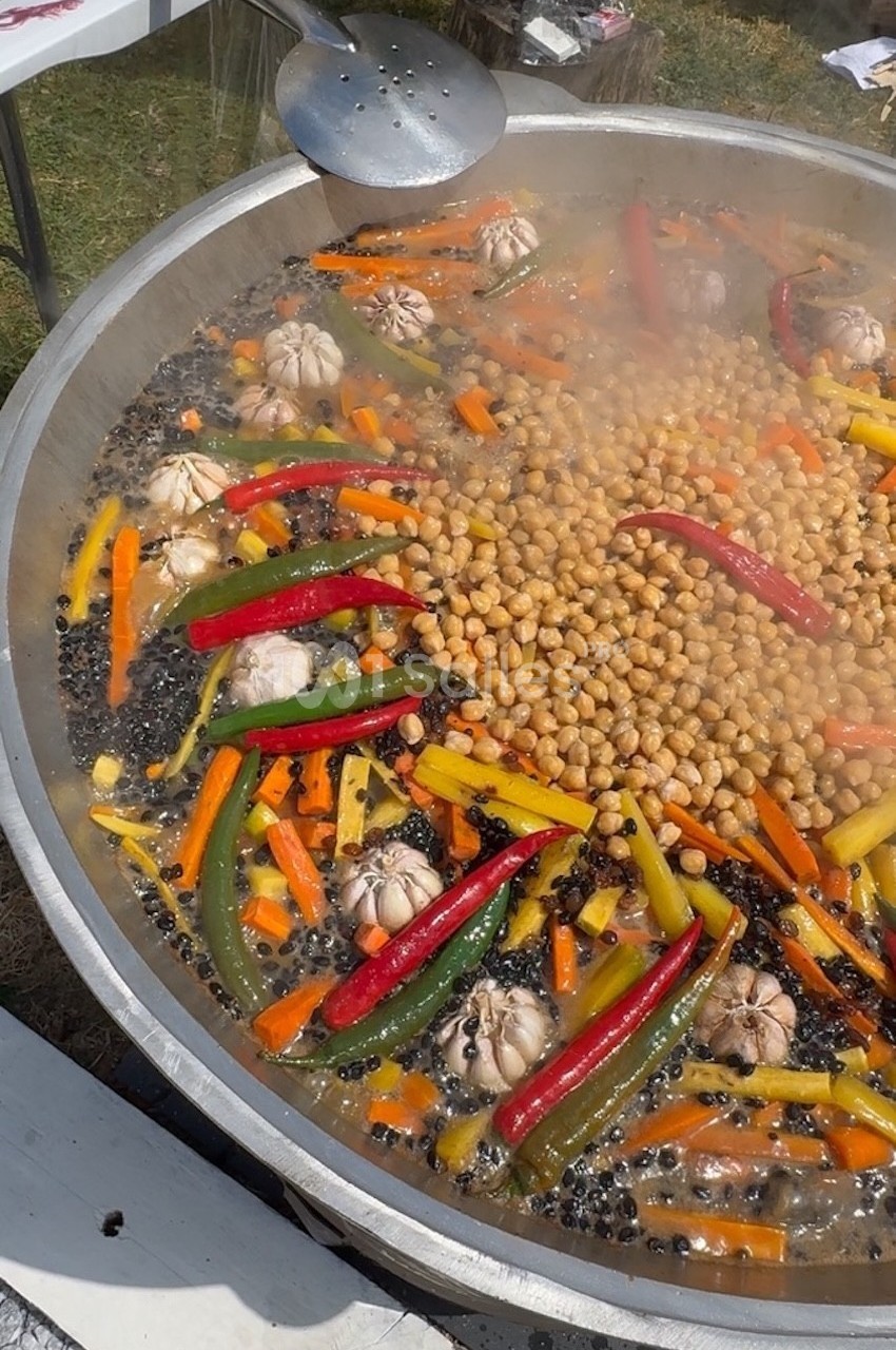 Grande poêle contenant pois chiches, carottes, poivrons, gousses d'ail et épices en cuisson à l'extérieur.