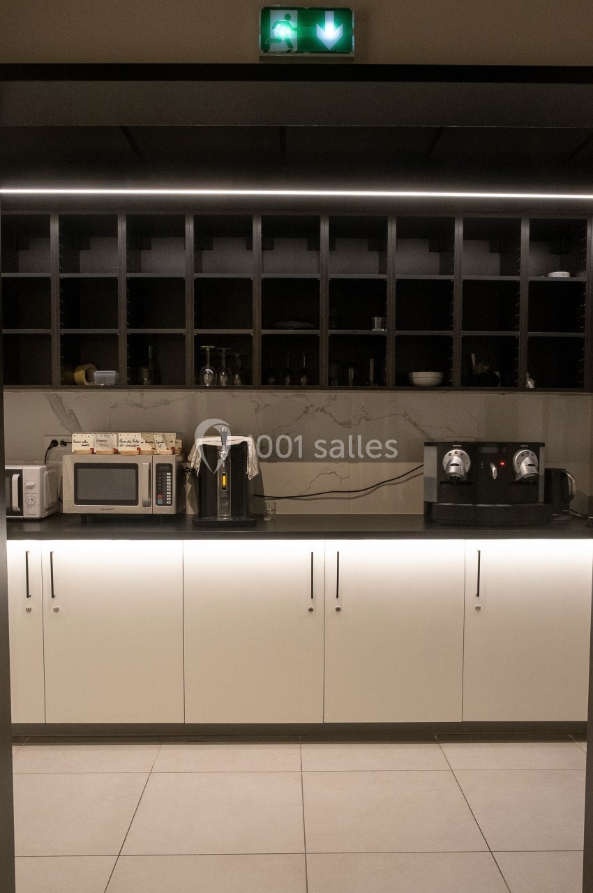 Cuisine moderne avec rangements ouverts, micro-ondes, cafetières et éclairage intégré sous les placards.