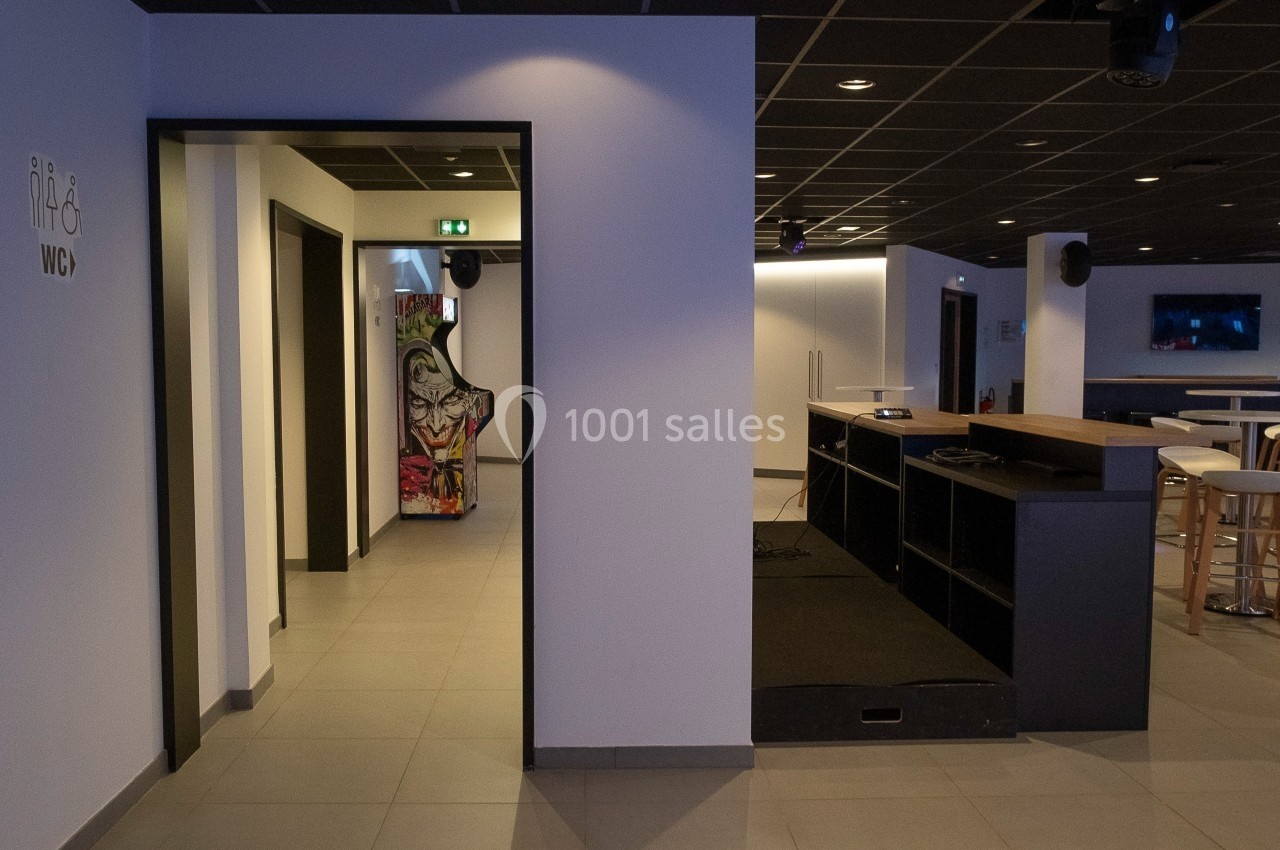 Espace intérieur moderne avec un comptoir, des tables hautes et un couloir menant à des toilettes signalées.