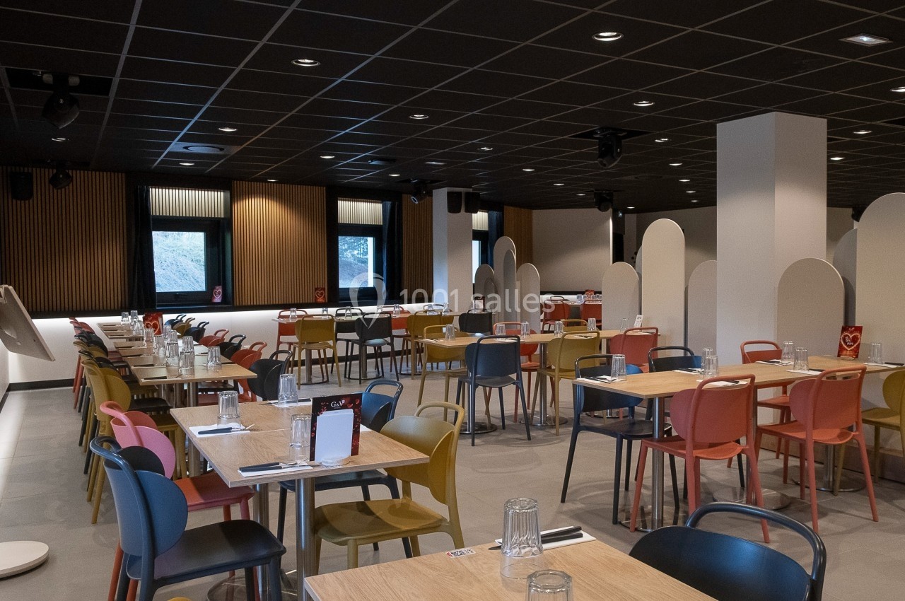 Salle de restaurant moderne avec tables en bois, chaises colorées et cloisons séparatrices sous un plafond sombre.