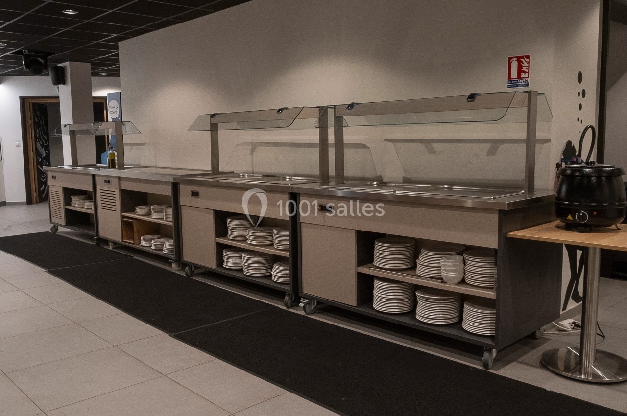 Buffet en libre-service avec comptoirs en inox, étagères contenant des assiettes et soupière sur une table à droite.