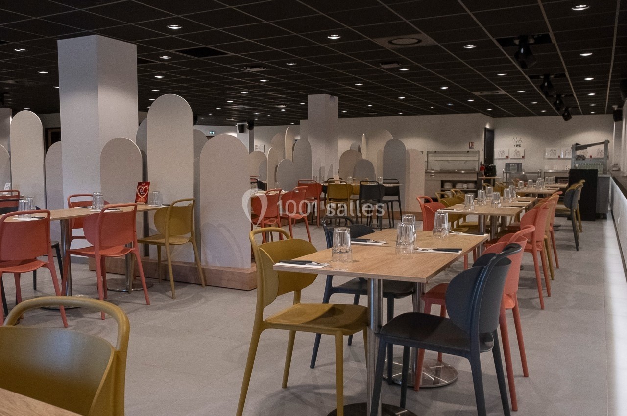 Salle de restaurant moderne avec des tables en bois, chaises colorées et cloisons séparatives blanches.