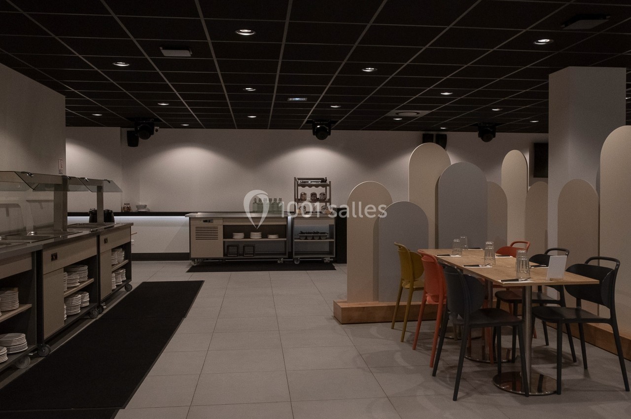 Salle de restauration moderne avec tables, chaises colorées, buffet en libre-service et cloisons décoratives.