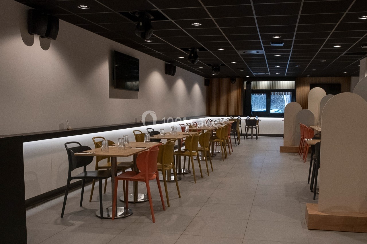 Salle de restaurant moderne avec tables alignées, chaises colorées et éclairage tamisé.