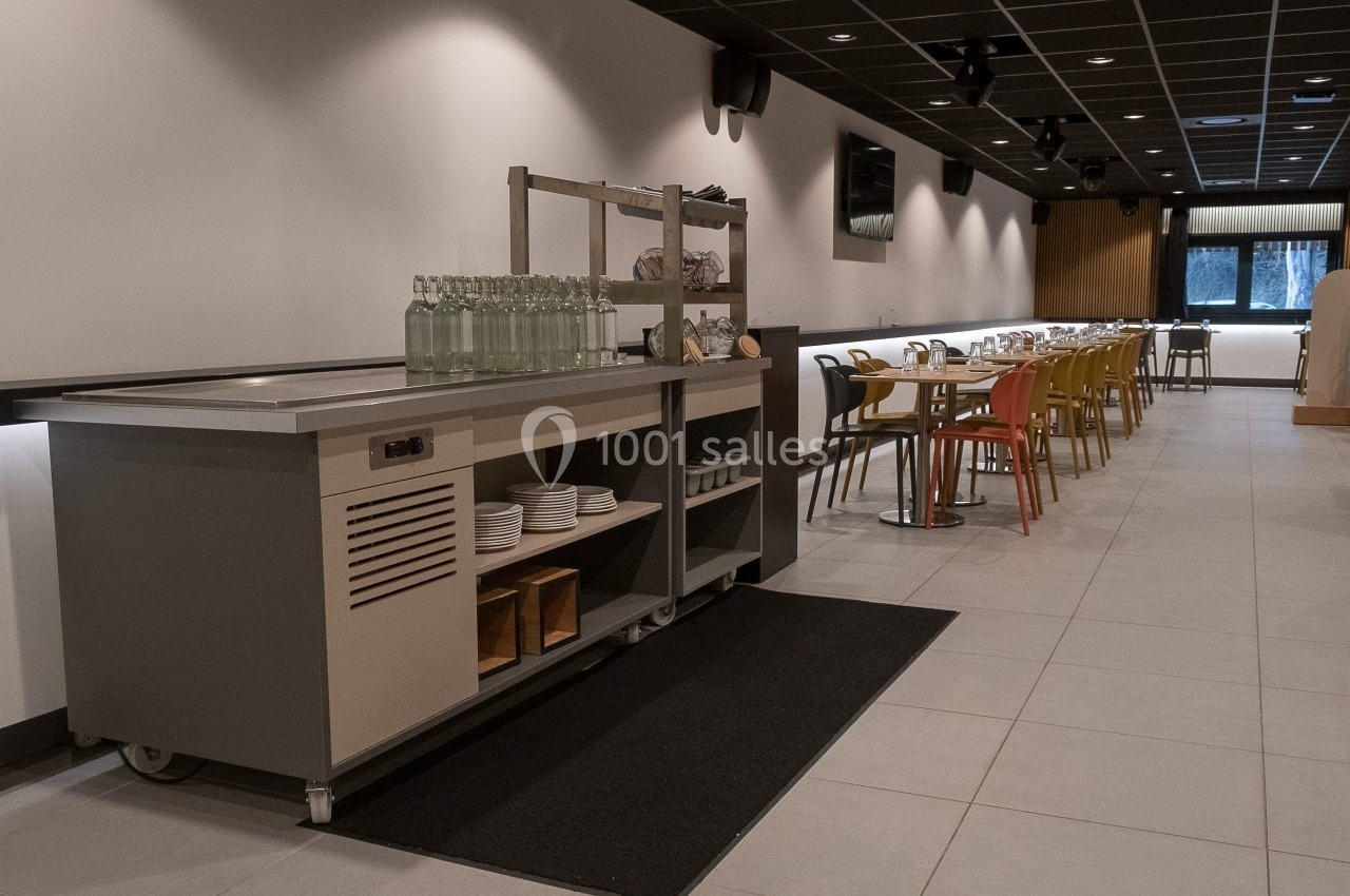 Salle de restaurant moderne avec tables alignées, chaises colorées et un buffet équipé de rangements au premier plan.