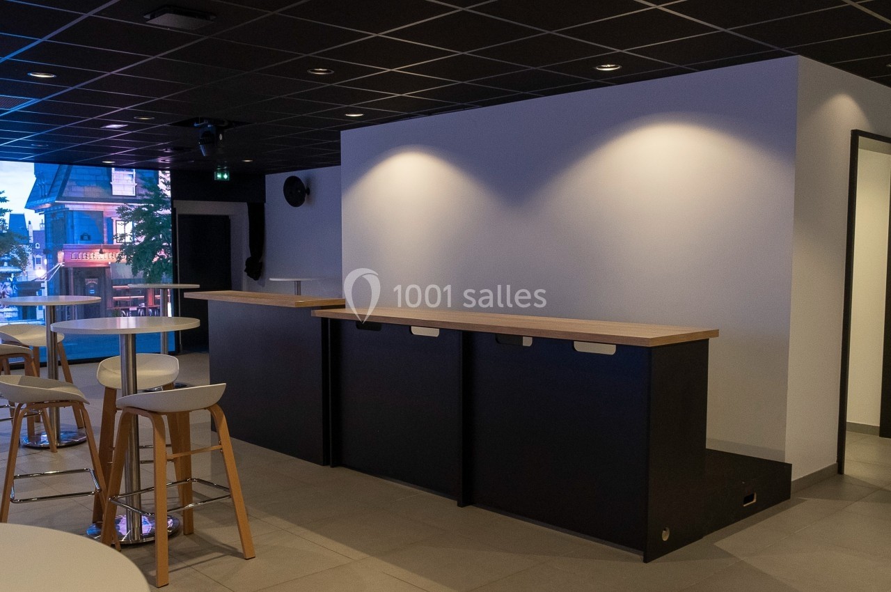 Espace intérieur moderne avec comptoir en bois, tabourets hauts et éclairage tamisé dans un cadre épuré.