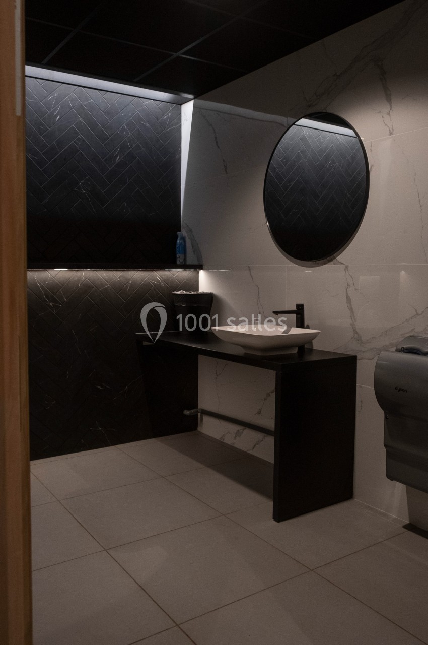Salle de bain moderne avec lavabo, miroir rond, mur en marbre et carrelage noir, éclairage intégré.
