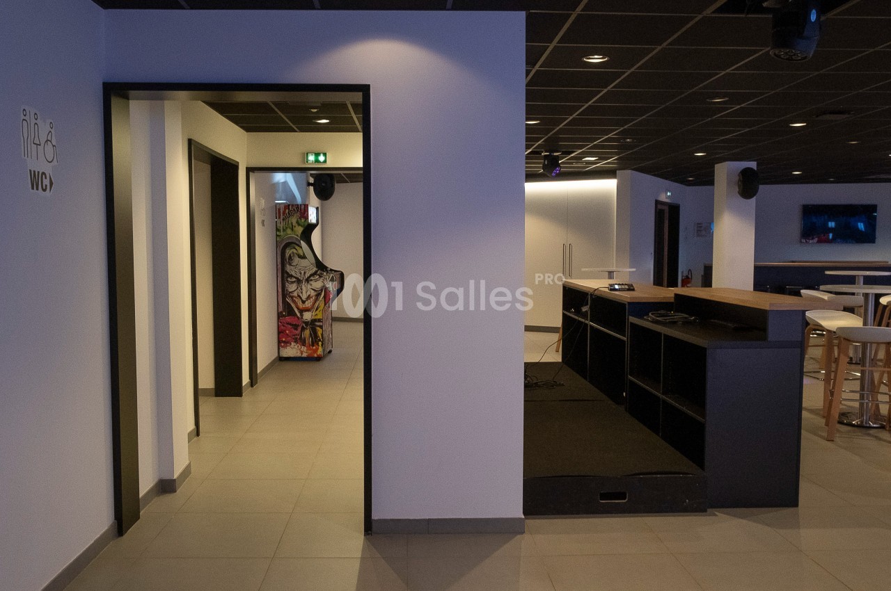 Espace intérieur moderne avec un sol carrelé, un comptoir, des tables hautes et une signalisation pour les toilettes.
