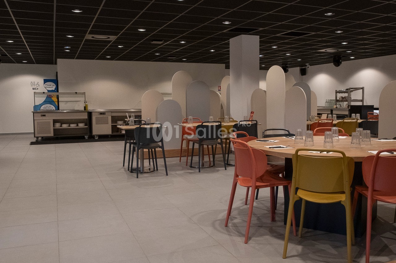 Salle de restaurant moderne avec tables rondes, chaises colorées et séparateurs en panneaux clairs.
