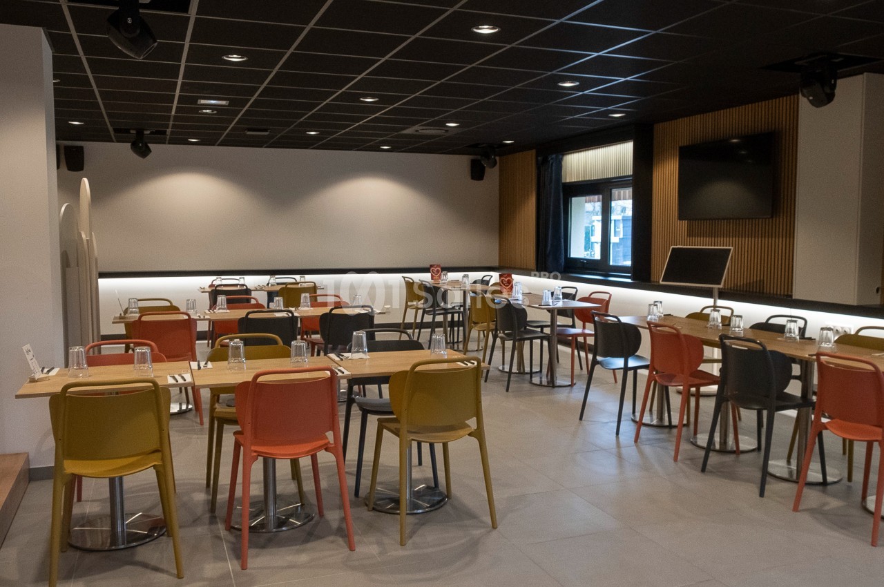 Salle de restaurant moderne avec tables en bois, chaises colorées et éclairage tamisé.