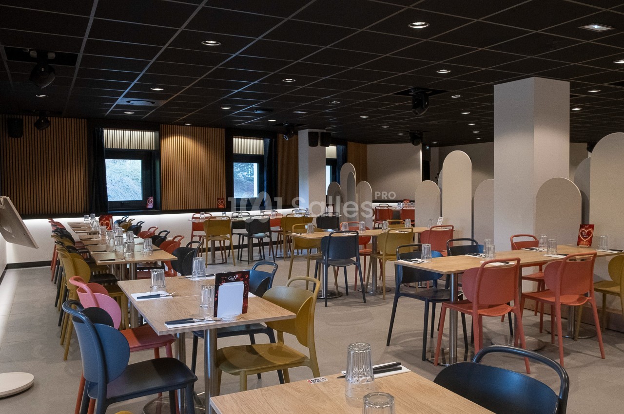 Salle de restaurant moderne avec des tables en bois, chaises colorées et cloisons blanches pour séparer les espaces.