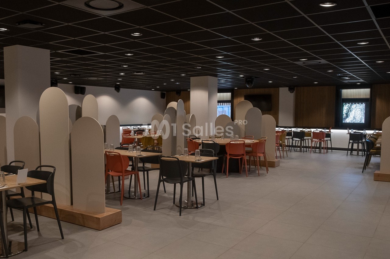 Salle de restaurant moderne avec tables, chaises colorées et séparateurs décoratifs sous un plafond sombre.
