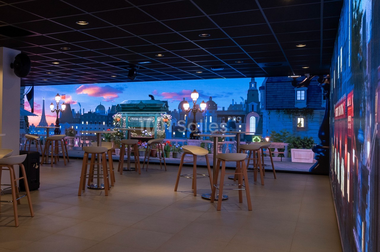 Salle moderne avec des tables hautes et un écran mural affichant une vue urbaine au coucher du soleil.