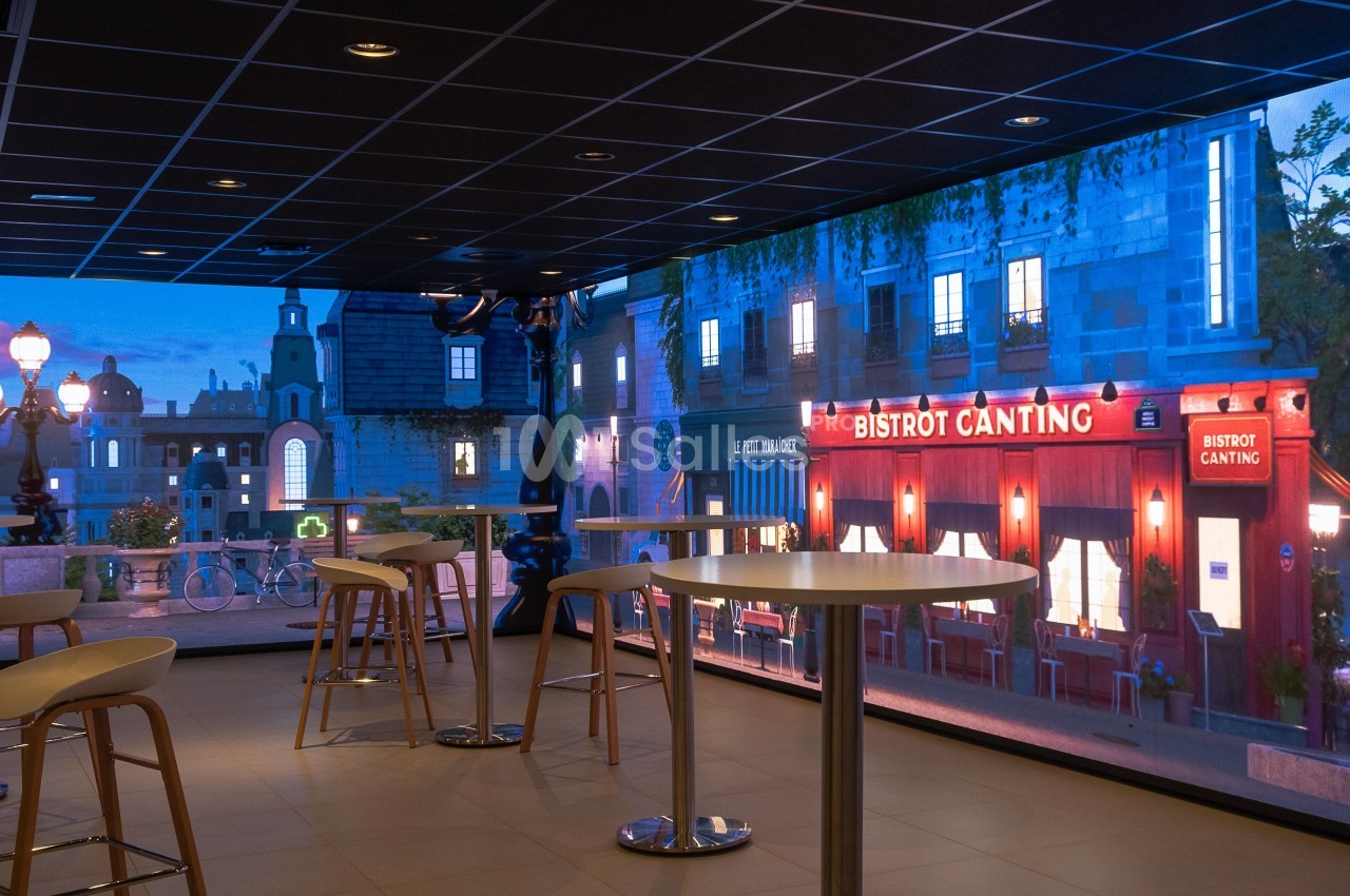 Salle moderne avec tables hautes et vue sur une façade de bistrot éclairée dans une ambiance nocturne.