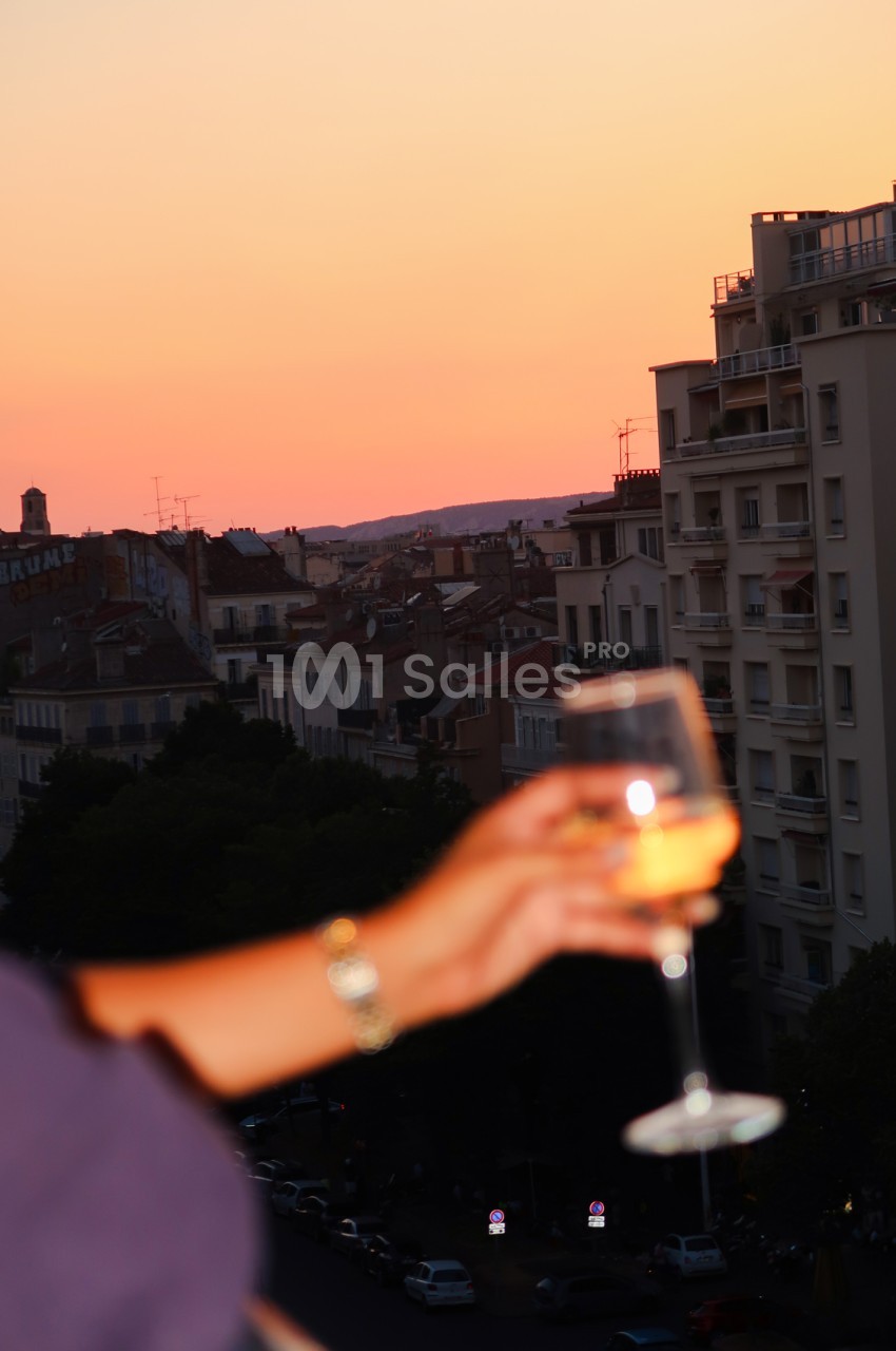 Verre de cocktail en premier plan, vue sur les toits de Marseille au coucher de soleil.