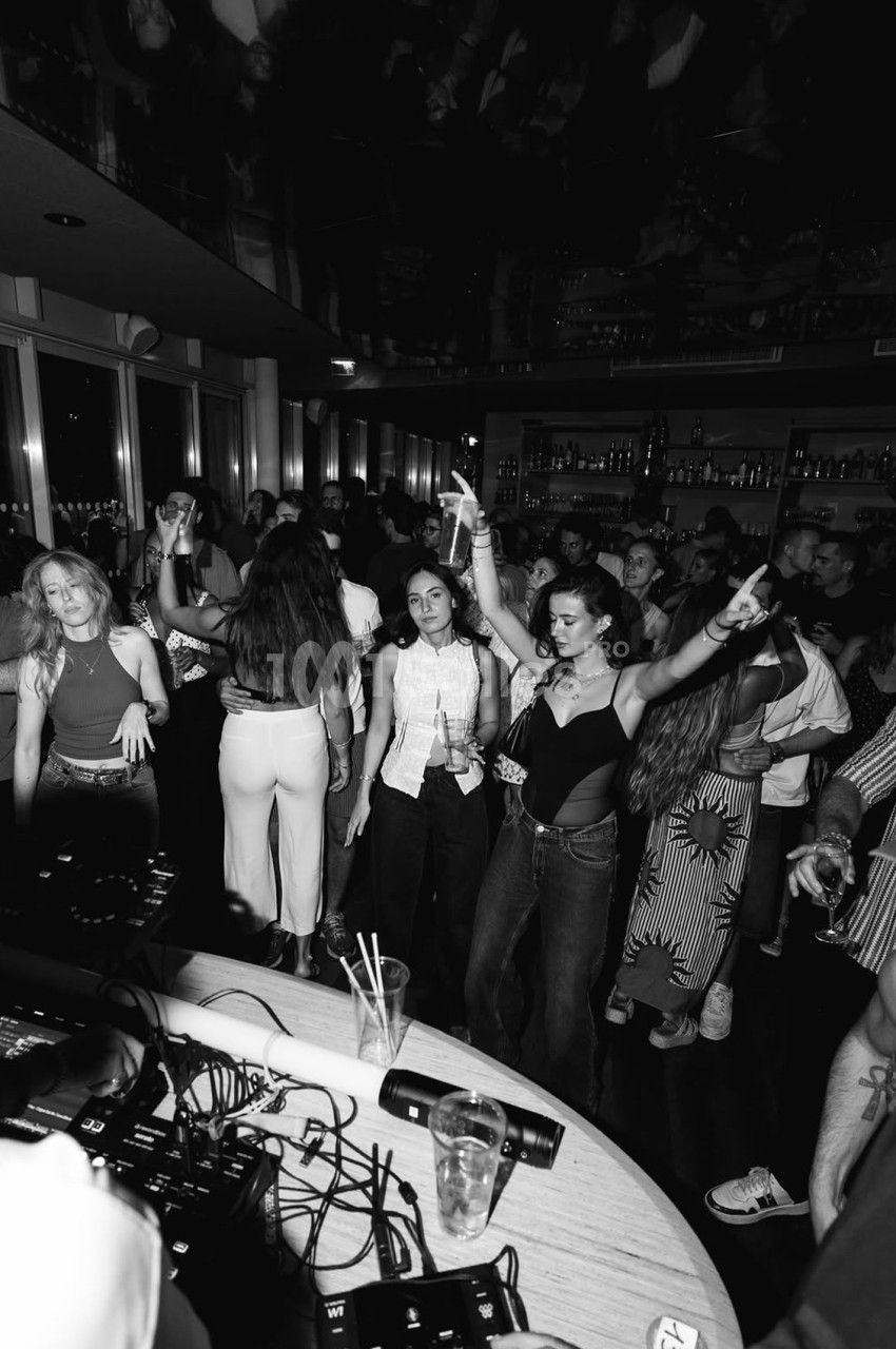 Salle de réception avec piste de danse bondée de convives en soirée, bar éclairé en arrière-plan.