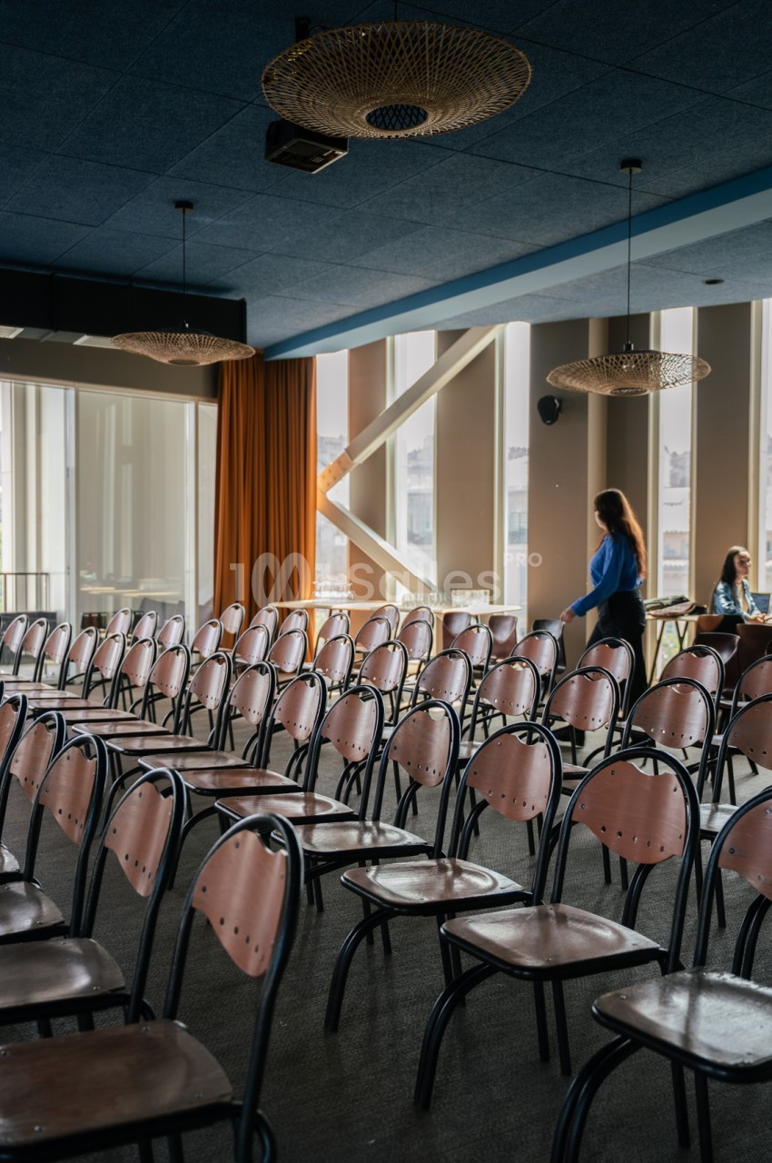 Salle de conférence avec rangées de chaises en métal et cuir rose face à des baies vitrées.