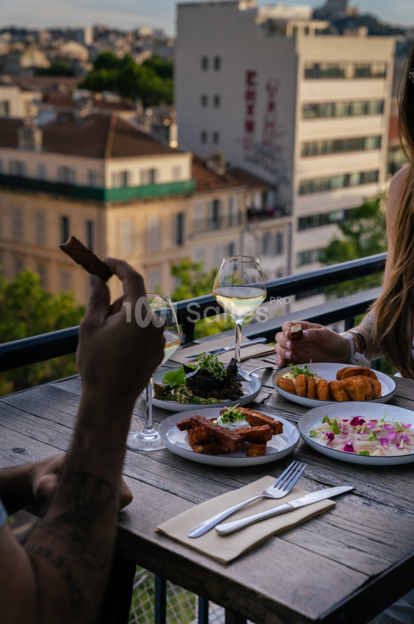 Table dressée sur une terrasse surplombant les toits de Marseille, avec verres de vin blanc et assiettes de cuisine gastronomique.