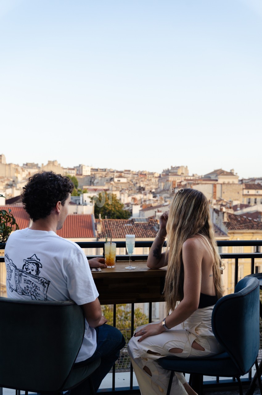 Deux personnes attablées sur une terrasse avec vue panoramique sur les toits de Marseille.