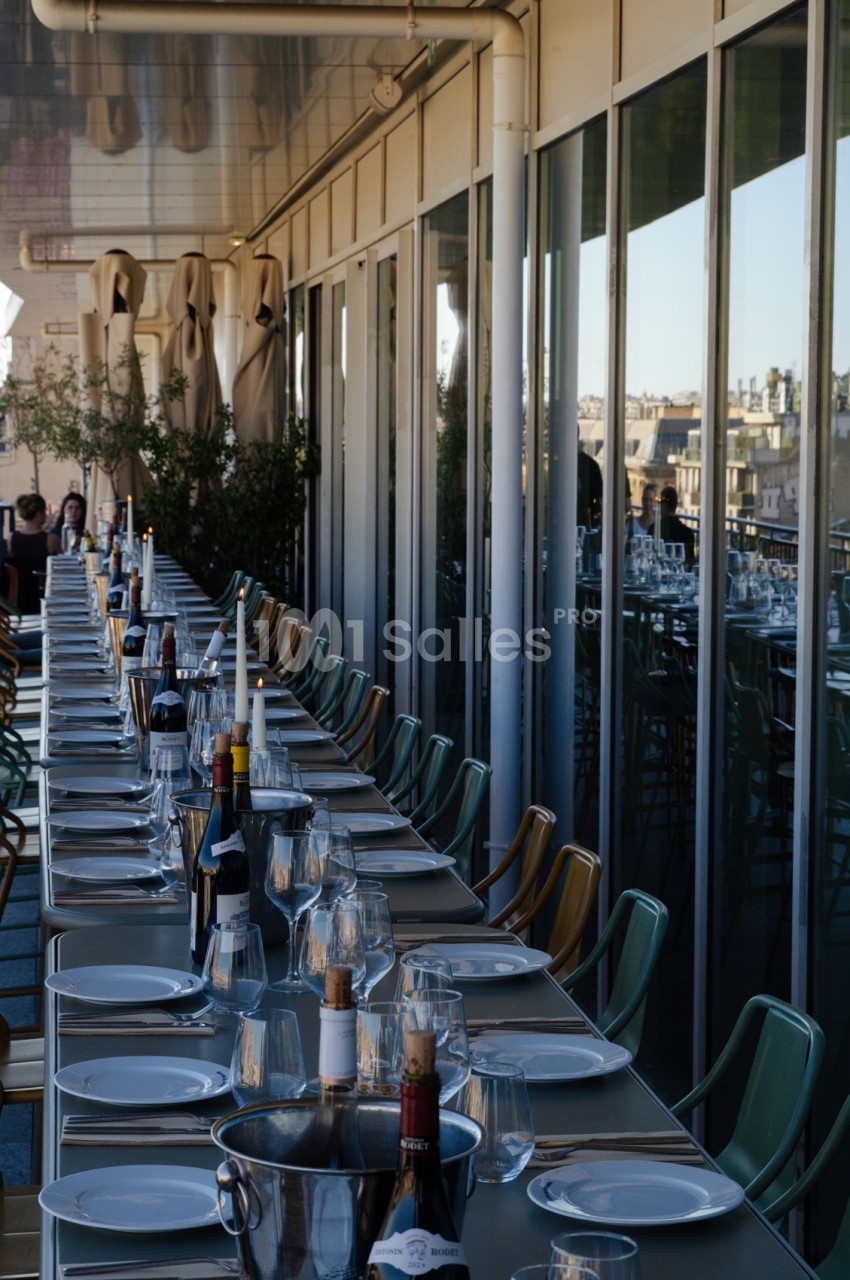 Terrasse sur toit avec tables dressées, chaises vertes, panorama urbain de Marseille en arrière-plan.