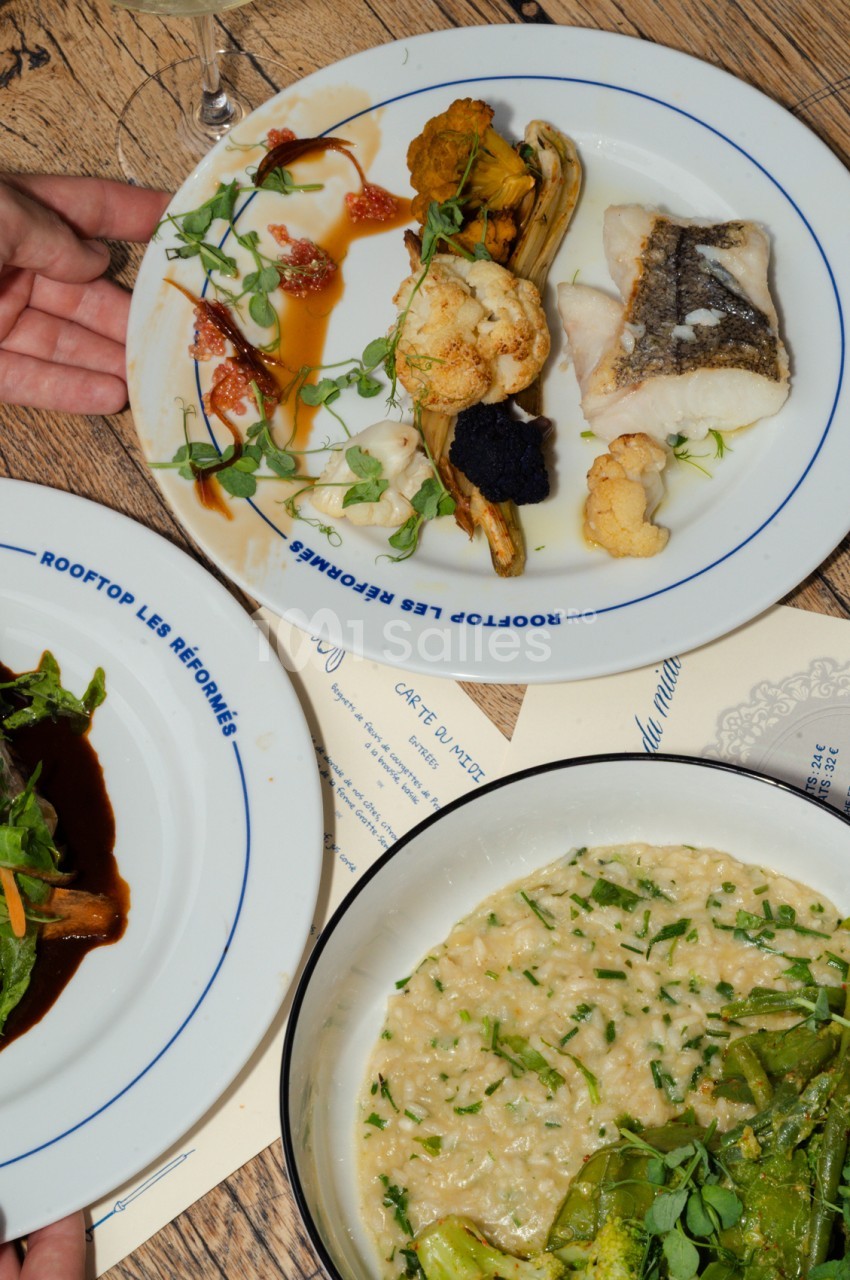 Assiettes dressées avec filet de poisson, œufs de poisson, légumes grillés et risotto sur table en bois.