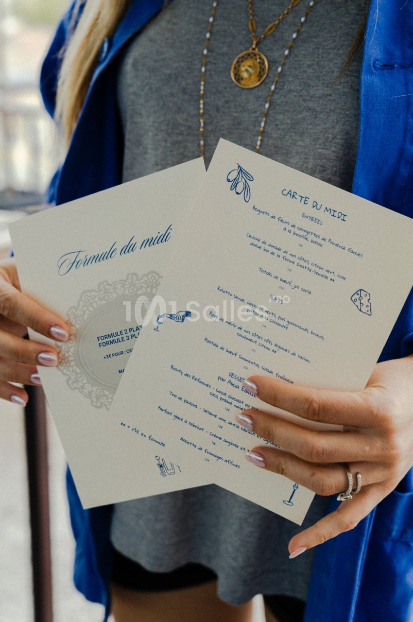 Personne tenant un menu imprimé bleu et crème avec illustrations culinaires - "Formule du midi" et "Carte du midi".