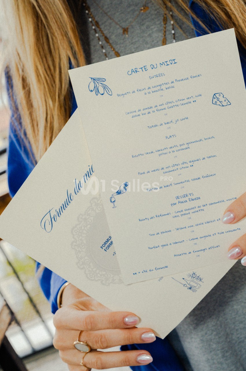 Personne tenant un menu manuscrit de réception aux sections entrées, plats et desserts ornés de dessins bleus.