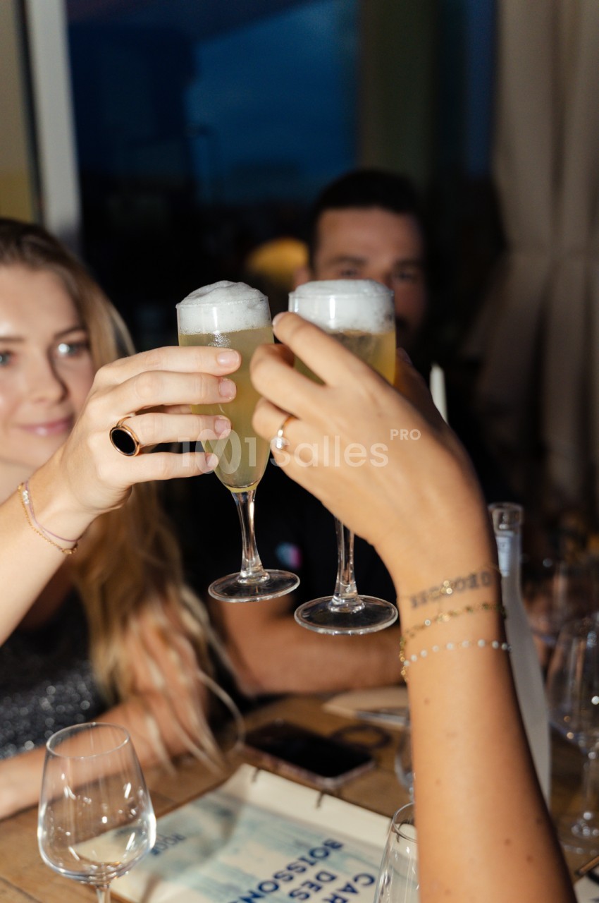 Deux convives trinquent avec des flûtes de champagne lors d'une soirée en intérieur.