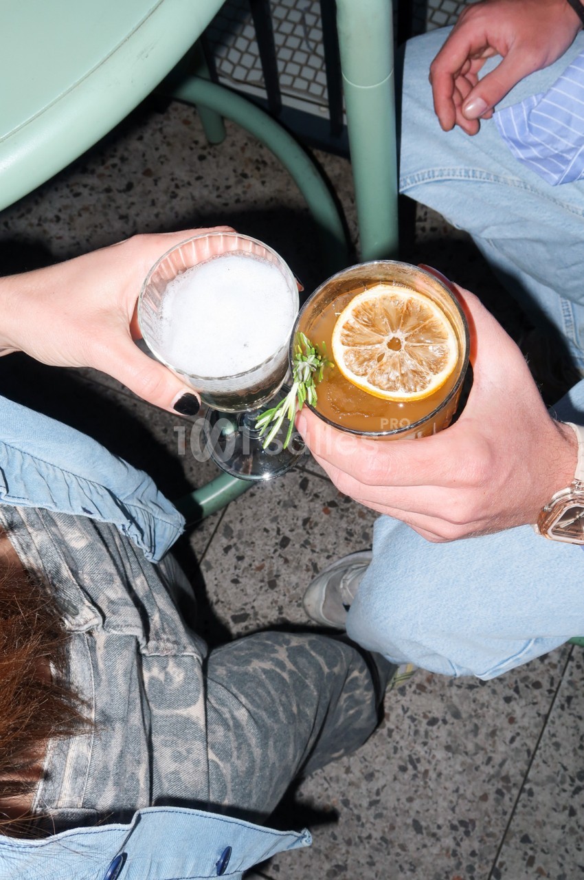 Deux personnes assises tiennent des verres - l'un contenant un cocktail blanc, l'autre un cocktail ambré garni de tranche de citron.