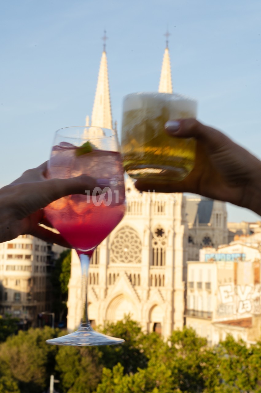 Deux verres de cocktails colorés levés en toast face à la basilique Notre-Dame de la Garde à Marseille.