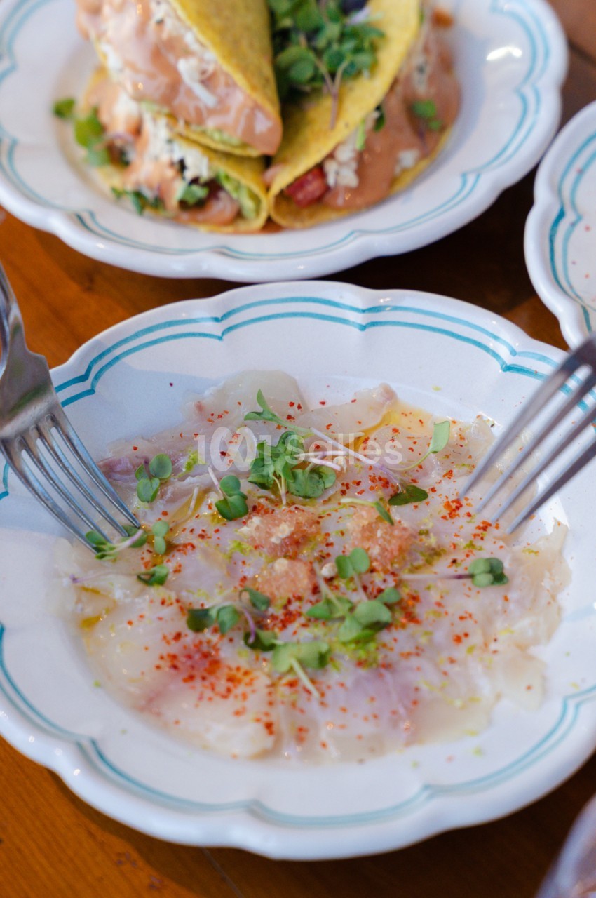 Ceviche de poisson blanc garni de piment d'Espelette et oignons verts sur assiette blanche.
