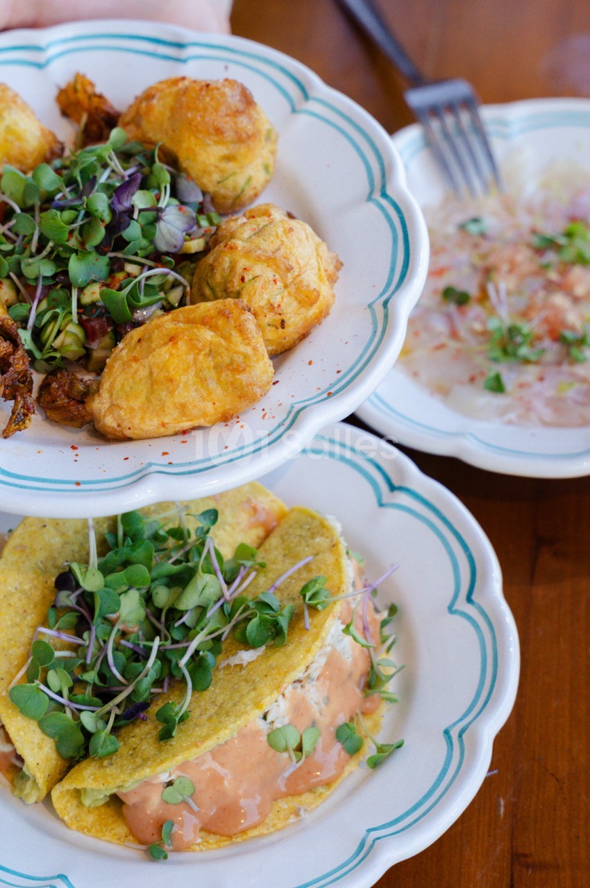 Assiettes blanches à liseret bleu contenant tacos garnis de saumon et pousses, et croquettes dorées avec salade.