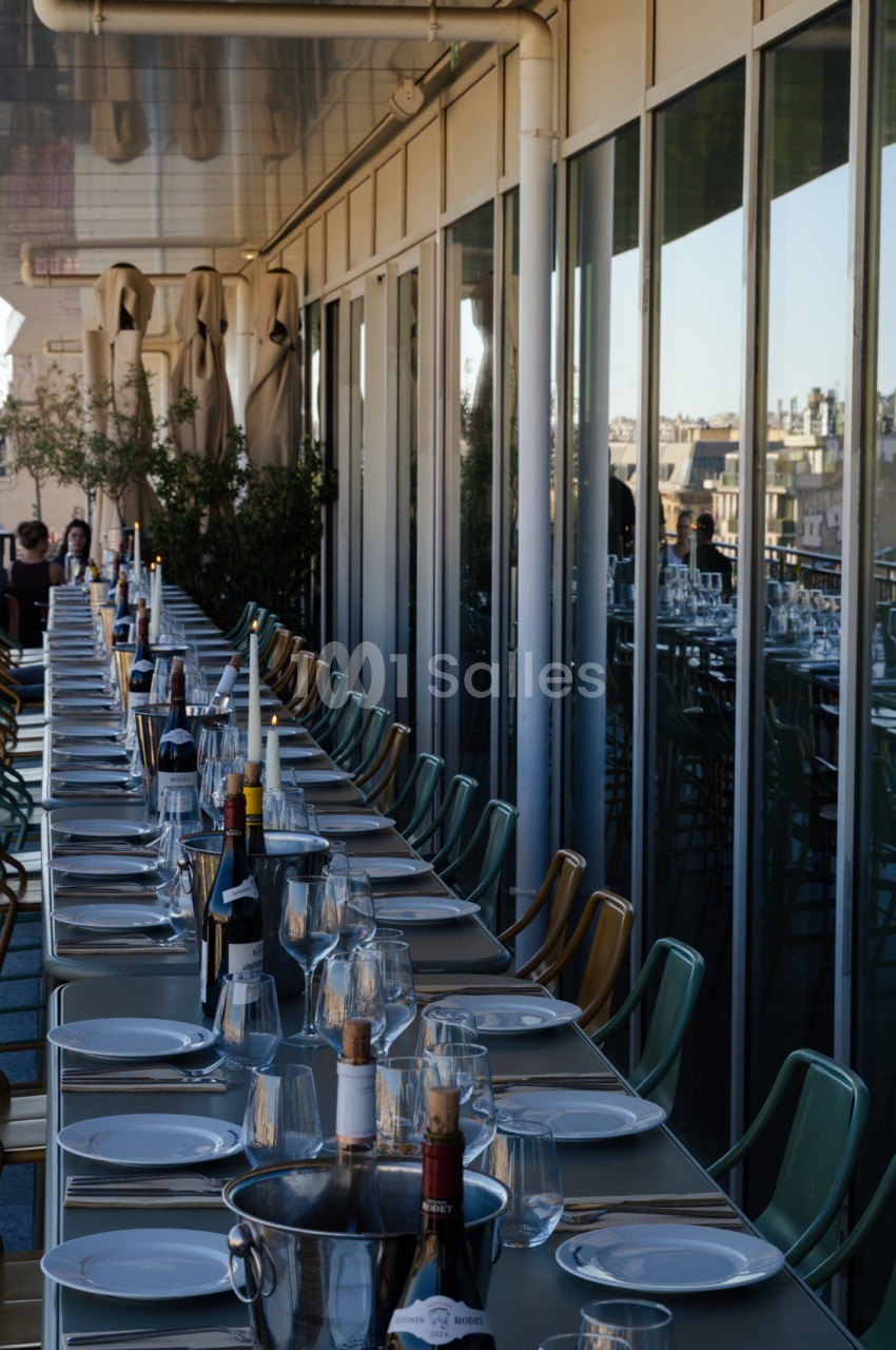 Terrasse sur toit avec tables dressées, chaises vertes, panorama urbain de Marseille en arrière-plan.