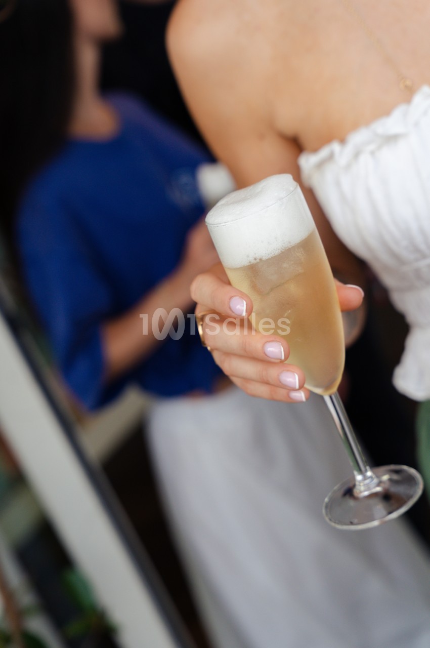 Verre de champagne tenu à la main lors d'un événement, invités en arrière-plan.