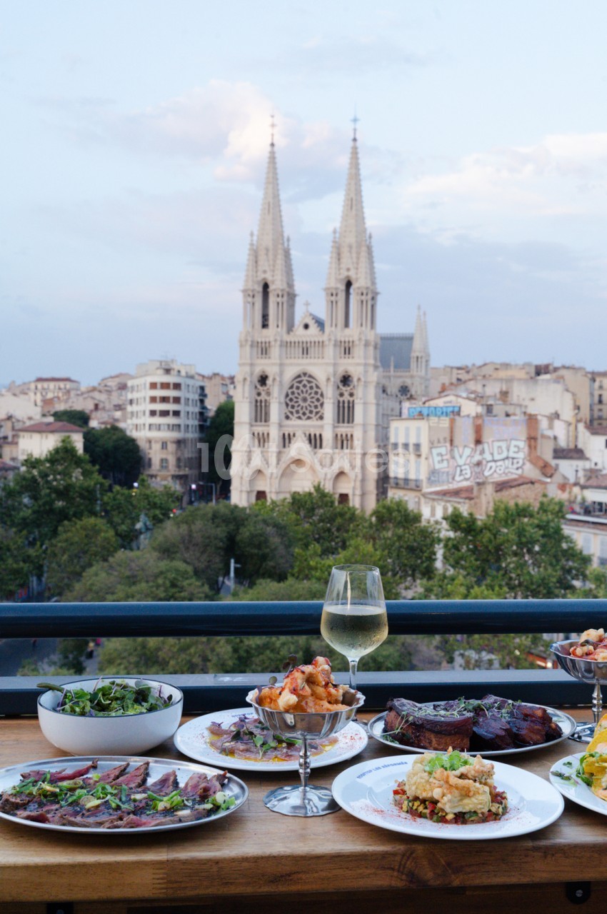 Table dressée avec assiettes, verres et plats - vue depuis une terrasse surplombant la basilique Notre-Dame-de-la-Garde.