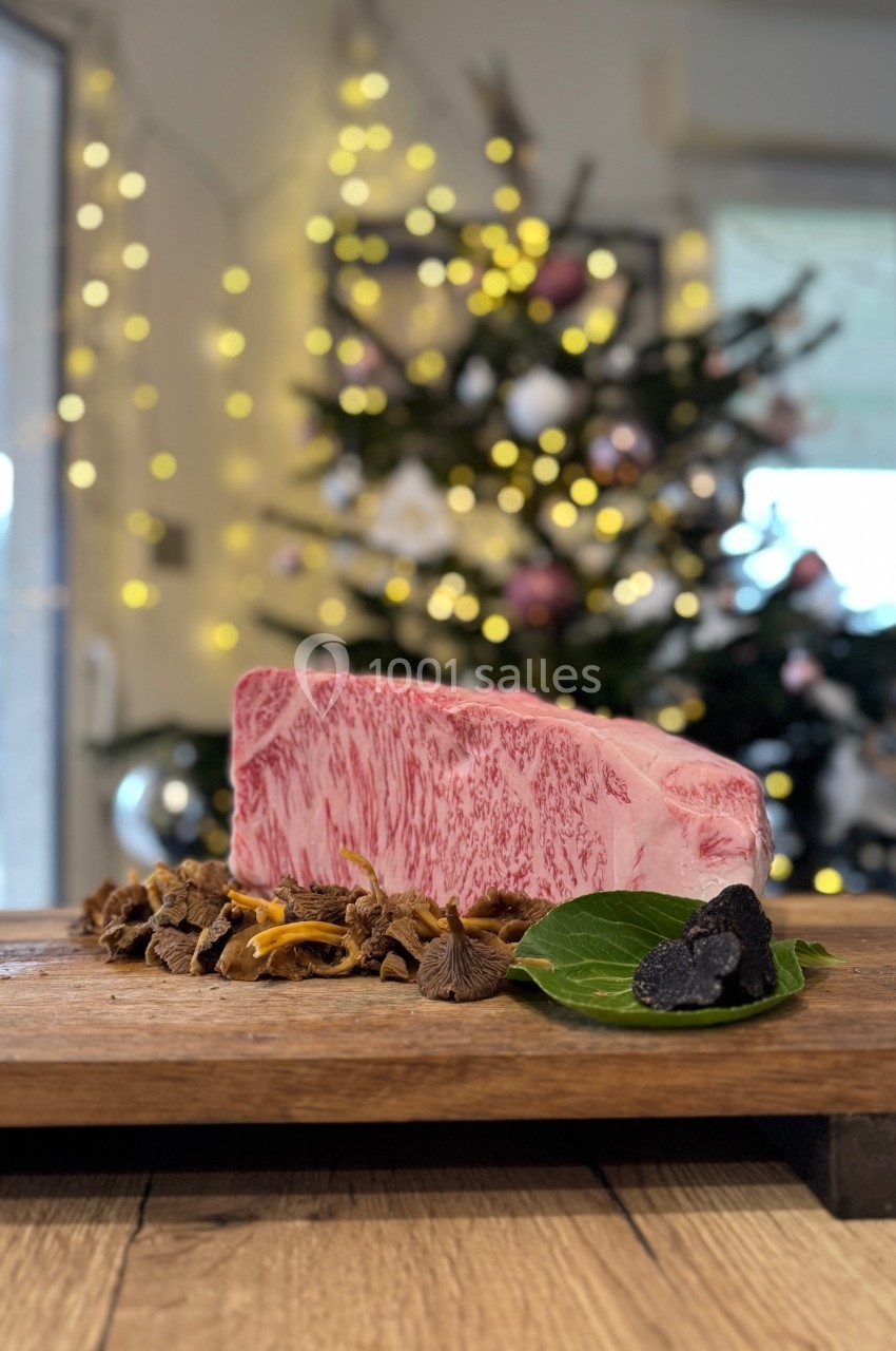 Morceau de viande marbrée posé sur une planche en bois avec des champignons, devant un sapin de Noël décoré.