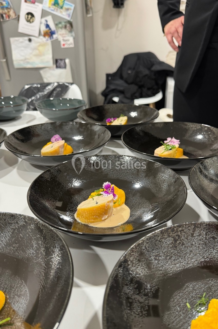 Assiettes noires contenant des plats élégants à base de purée orange, sauce et garniture florale, disposées sur une table.