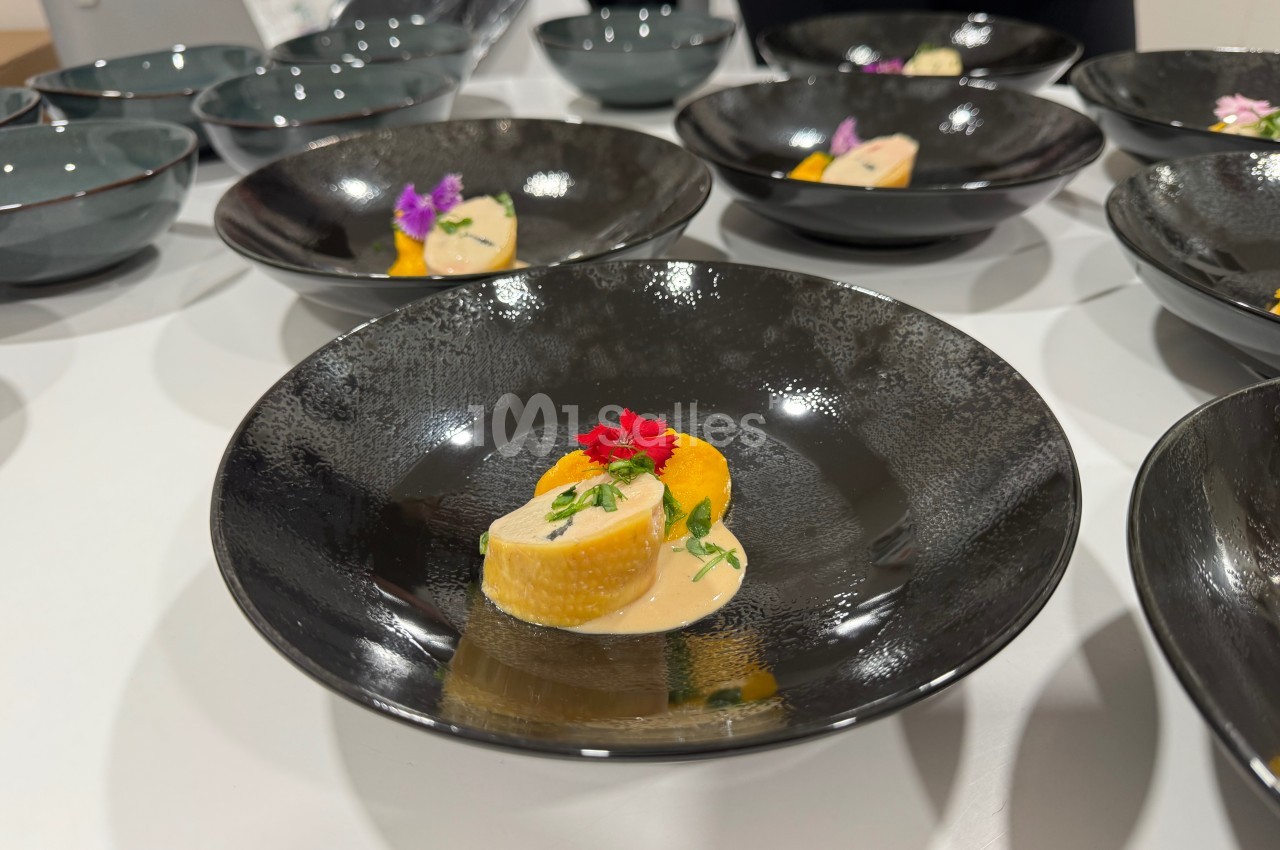 Assiette noire contenant une présentation soignée de légumes colorés, sauce crémeuse et décoration florale.