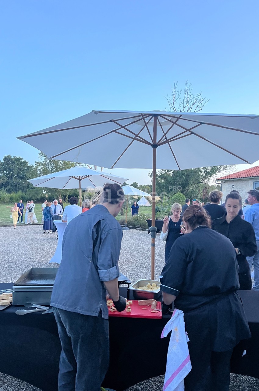 Des personnes se servent à un buffet en plein air sous des parasols, dans un cadre champêtre par temps clair.