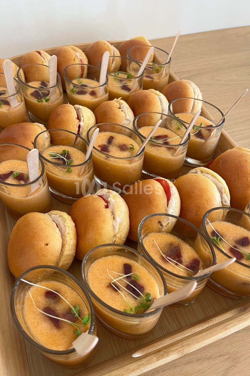 Plateau de mini-burgers et verrines de soupe garnies de fines herbes, présenté sur une table en bois.