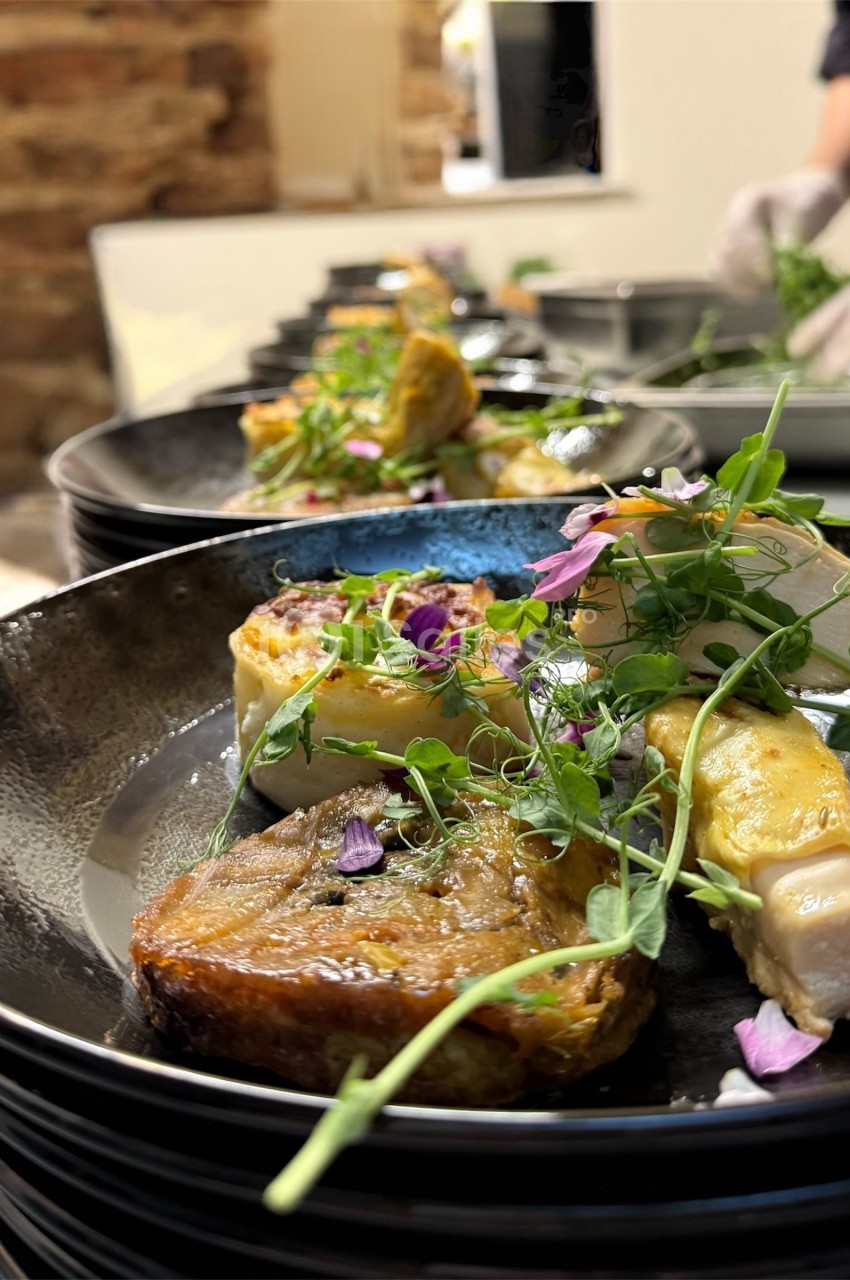 Assiette gastronomique avec viande, légumes, herbes fraîches et fleurs comestibles, servie en extérieur.