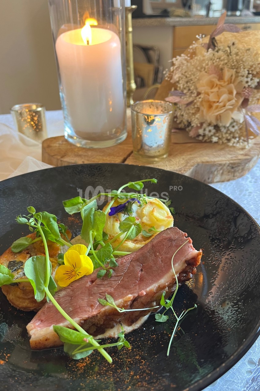 Assiette de viande grillée avec purée, légumes verts et fleurs comestibles, décorée dans un cadre élégant avec bougie.