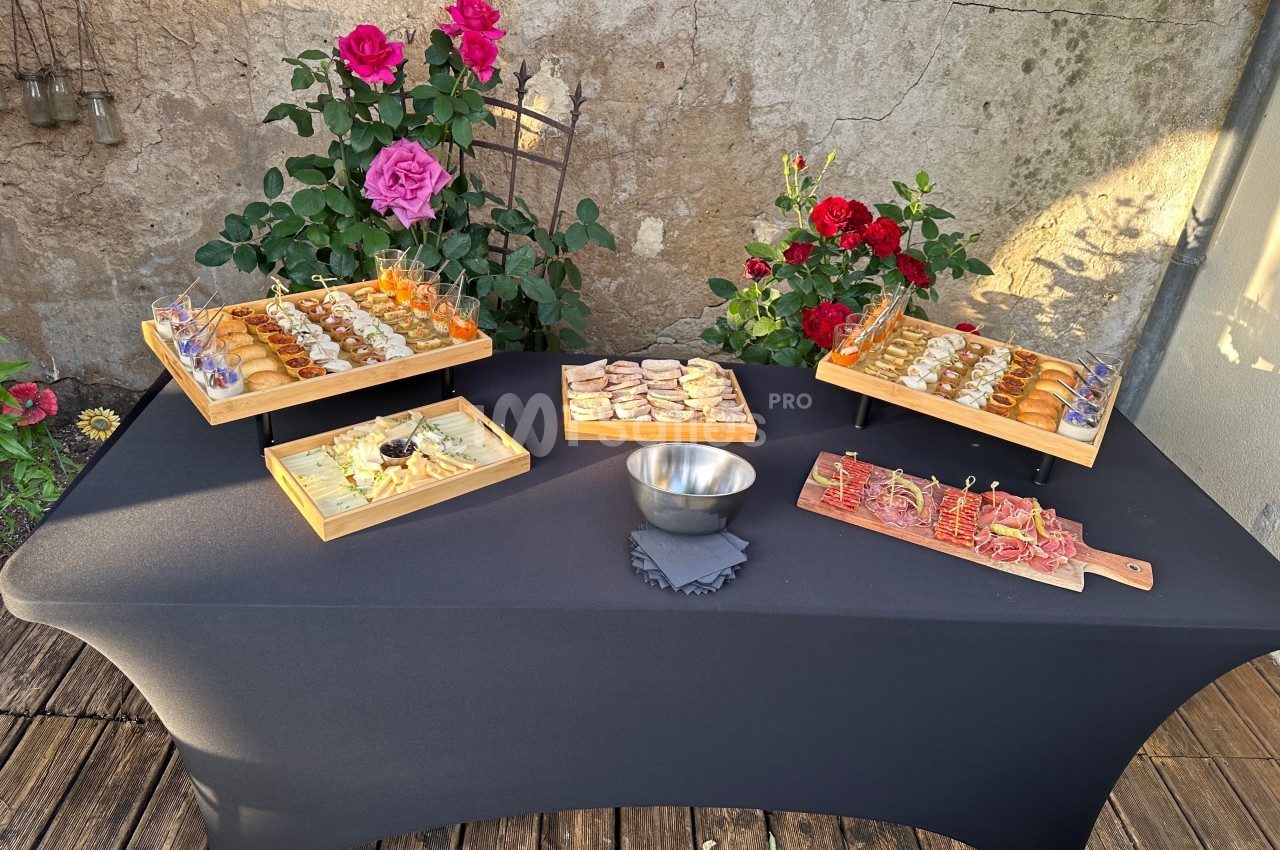 Buffet de bouchées apéritives variées disposées sur une table noire, entourée de rosiers en extérieur.